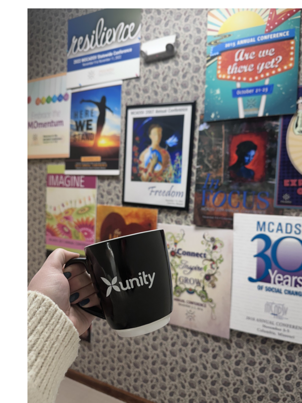 Black Unity mug in front of MOCADSV Conference posters